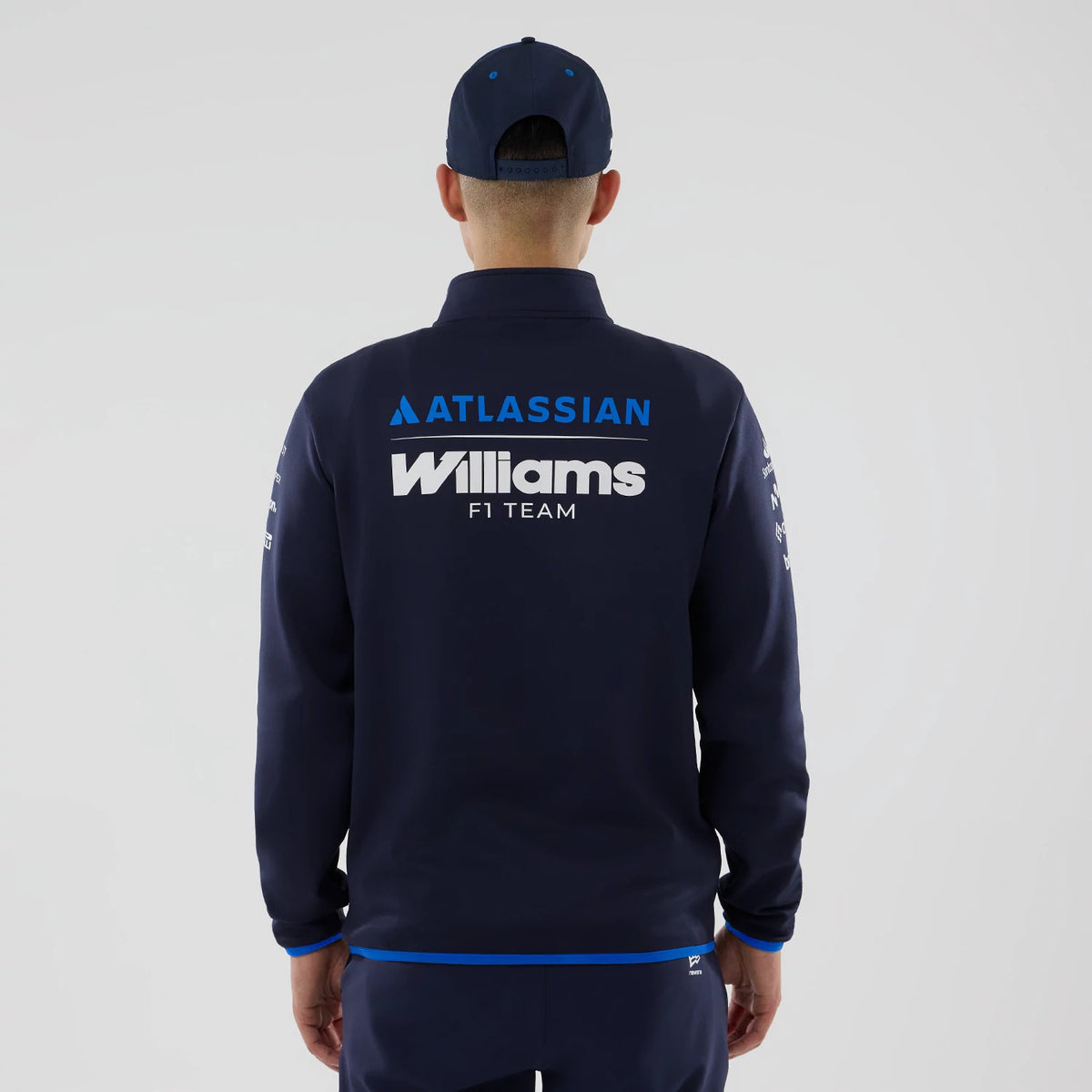 New Era Williams Navy Mid Layer 1/4 Zip Sweater, back view on a model wearing a navy cap, featuring prominent Atlassian and Williams F1 Team logos across the upper back and shoulders, with blue on cuffs and hem.
