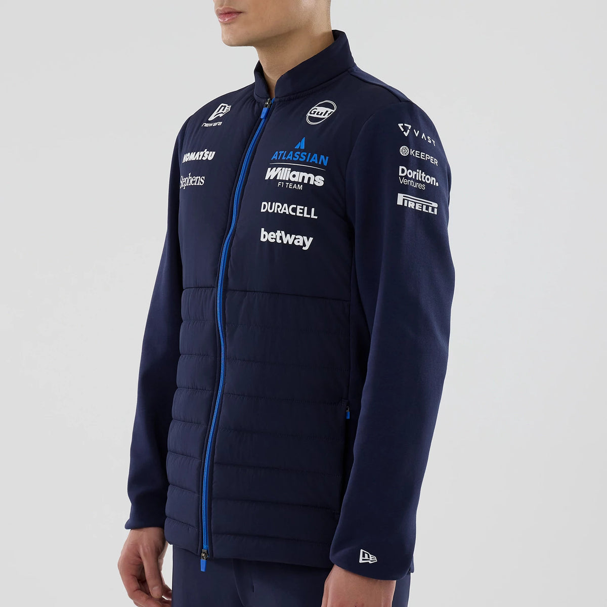 New Era Williams Navy Hybrid Jacket, three-quarter view on a model showcasing the blue zip closure, multiple sponsors' logos embroidered on the chest and sleeves, and a quilted panel design on the front with a New Era logo on the cuff.