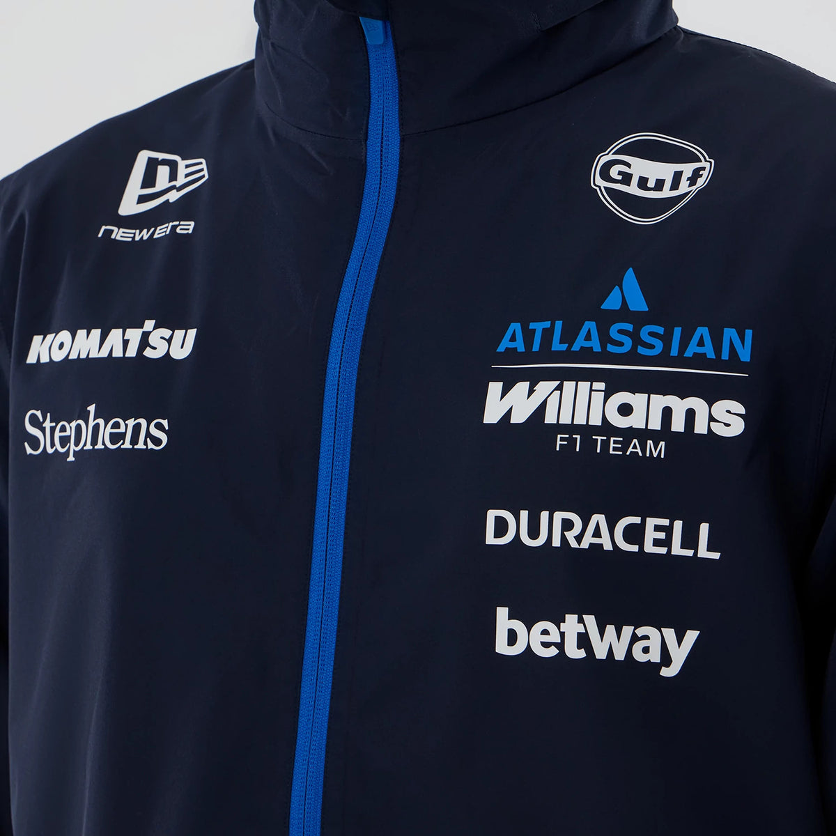 New Era Williams Navy Rain Jacket, front view showing a navy jacket with a blue zip running down the centre, various white sponsors' logos including Komatsu and Duracell, and an embroidered New Era logo on the left shoulder.