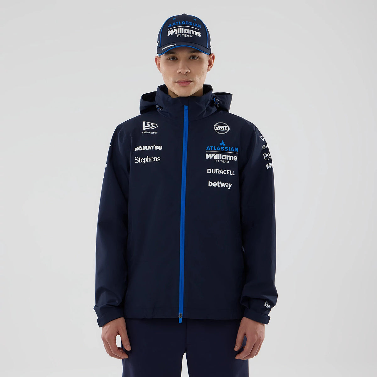 New Era Williams Navy Rain Jacket, front view on model with a matching cap, featuring prominent sponsor logos including Gulf and Atlassian on the chest, a full-length blue zip down the centre, and the New Era embroidered logo on the sleeve.