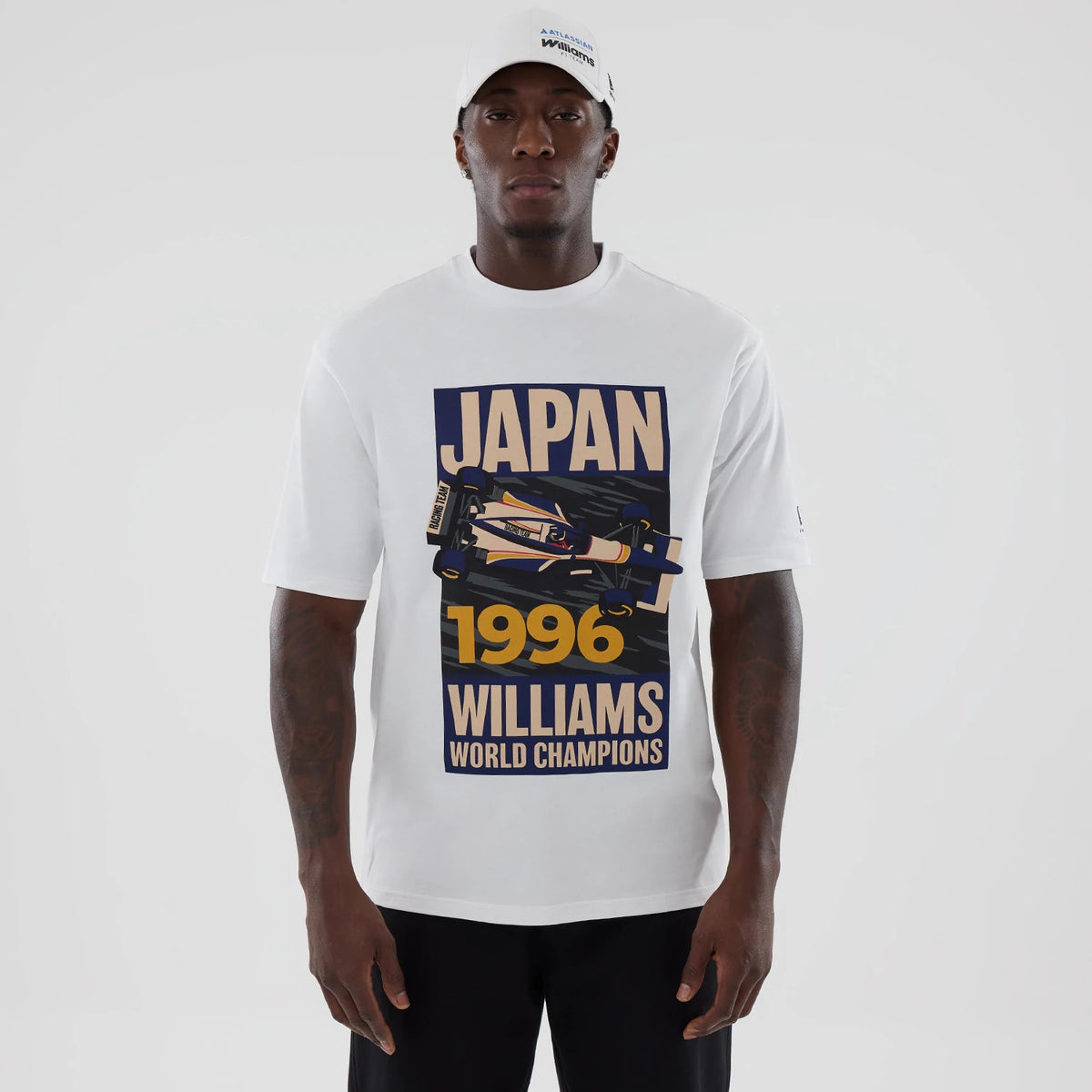 New Era Williams Japan 1996 White Oversized T-Shirt, front view on a model styled with a white cap, displaying a printed graphic of a race car with JAPAN 1996 WILLIAMS WORLD CHAMPIONS lettering prominently across the chest.