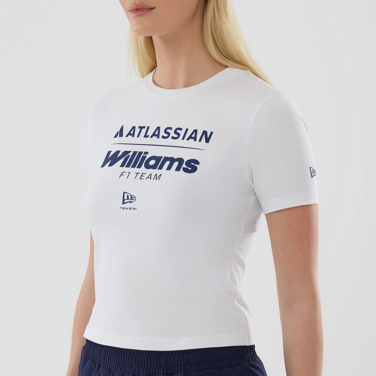 New Era Williams Womens White T-Shirt, front three-quarter view depicting a model wearing the shirt with navy Atlassian and Williams F1 Team logos printed across the chest, a small New Era logo printed below, and a secondary logo on the left sleeve.