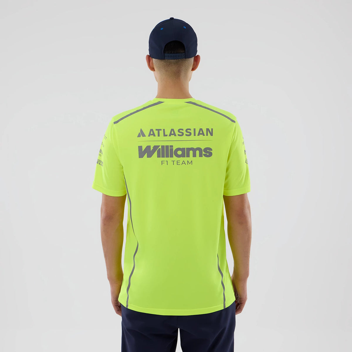 New Era Williams Set Up Yellow T-Shirt, back view on-model showing Atlassian and Williams F1 Team printed lettering in grey across the upper back, grey stripe along the sleeves, paired with a dark cap and shorts.
