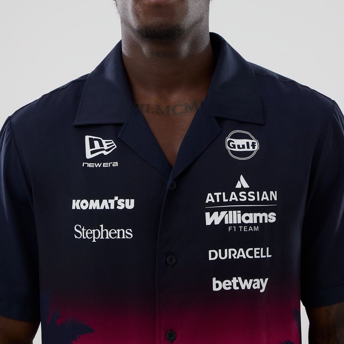 New Era Williams Miami Navy Short Sleeve Shirt, front view on a model featuring multiple sponsor logos including New Era, Komatsu, and Gulf on the chest, with a gradient design from navy to red at the lower part of the shirt.