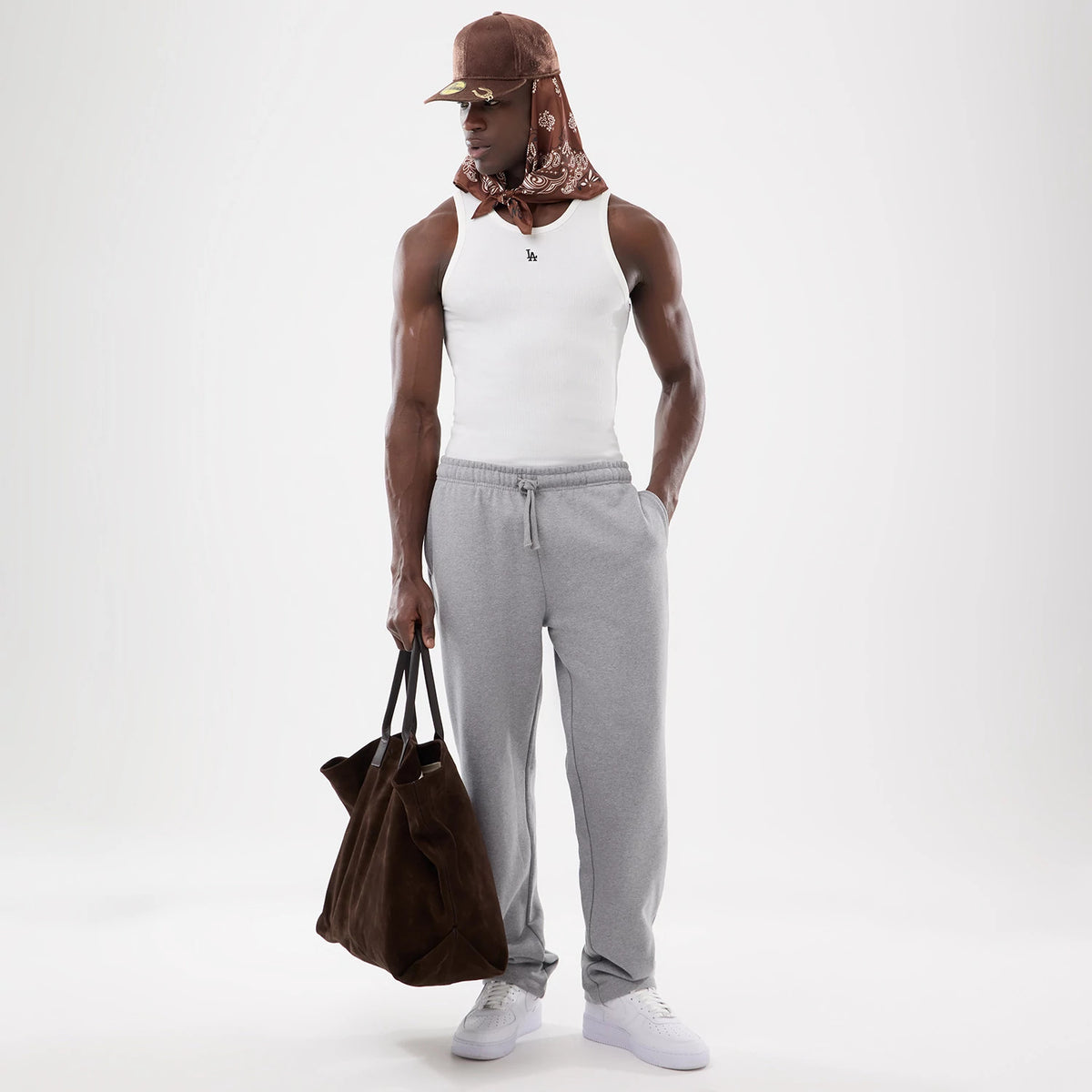 New Era LA Dodgers MLB Rib White Vest, front view on a model paired with grey drawstring sweatpants and a brown cap with matching patterned scarf, showing the small embroidered Dodgers logo on the front of the white ribbed vest.