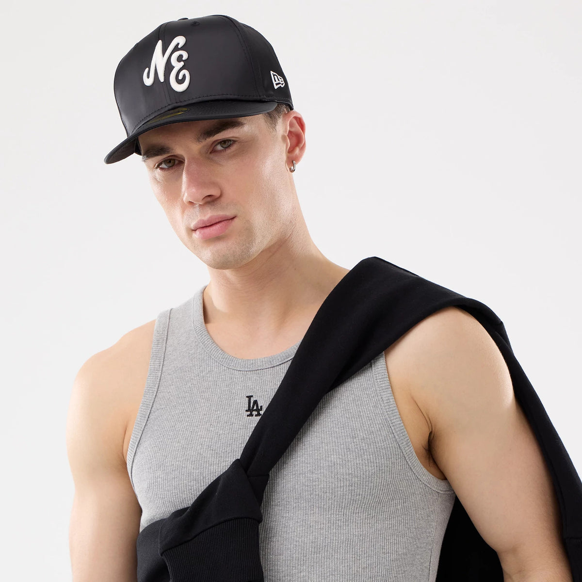 New Era LA Dodgers MLB Rib Grey Vest, on-model view with a grey ribbed vest featuring the LA logo embroidered on the chest, paired with a black cap showing a white NE logo and a black jacket draped over the shoulder.