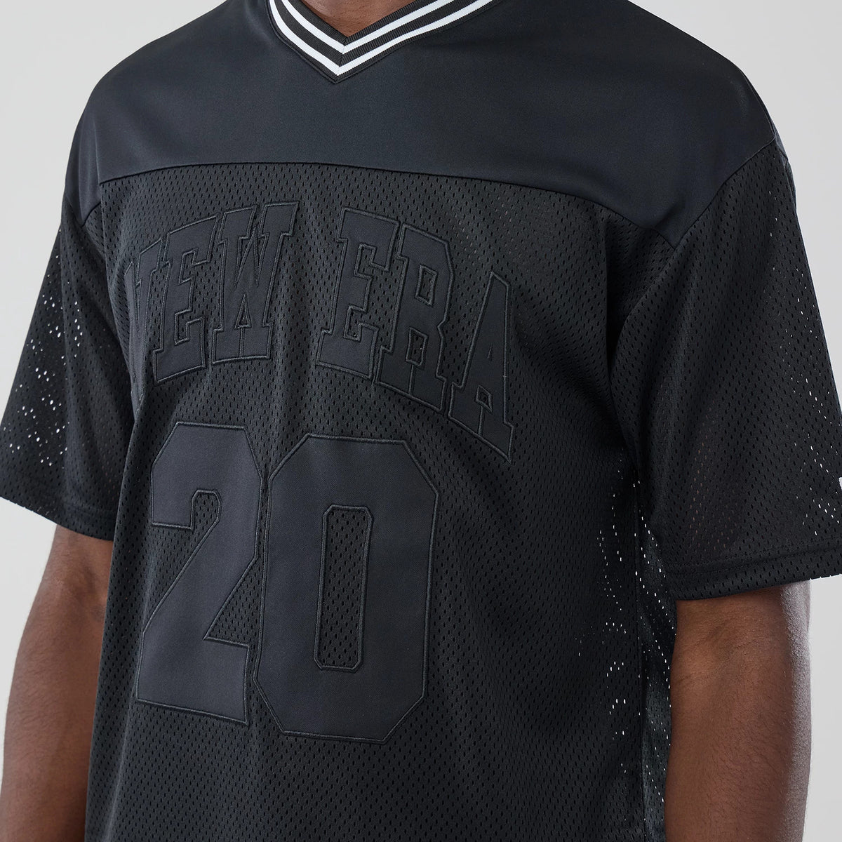 New Era Mesh Black Oversized T-Shirt, front view showing the raised New Era lettering across the chest, large number 20 below it, and the contrasting striped V-neck collar on the black mesh fabric.