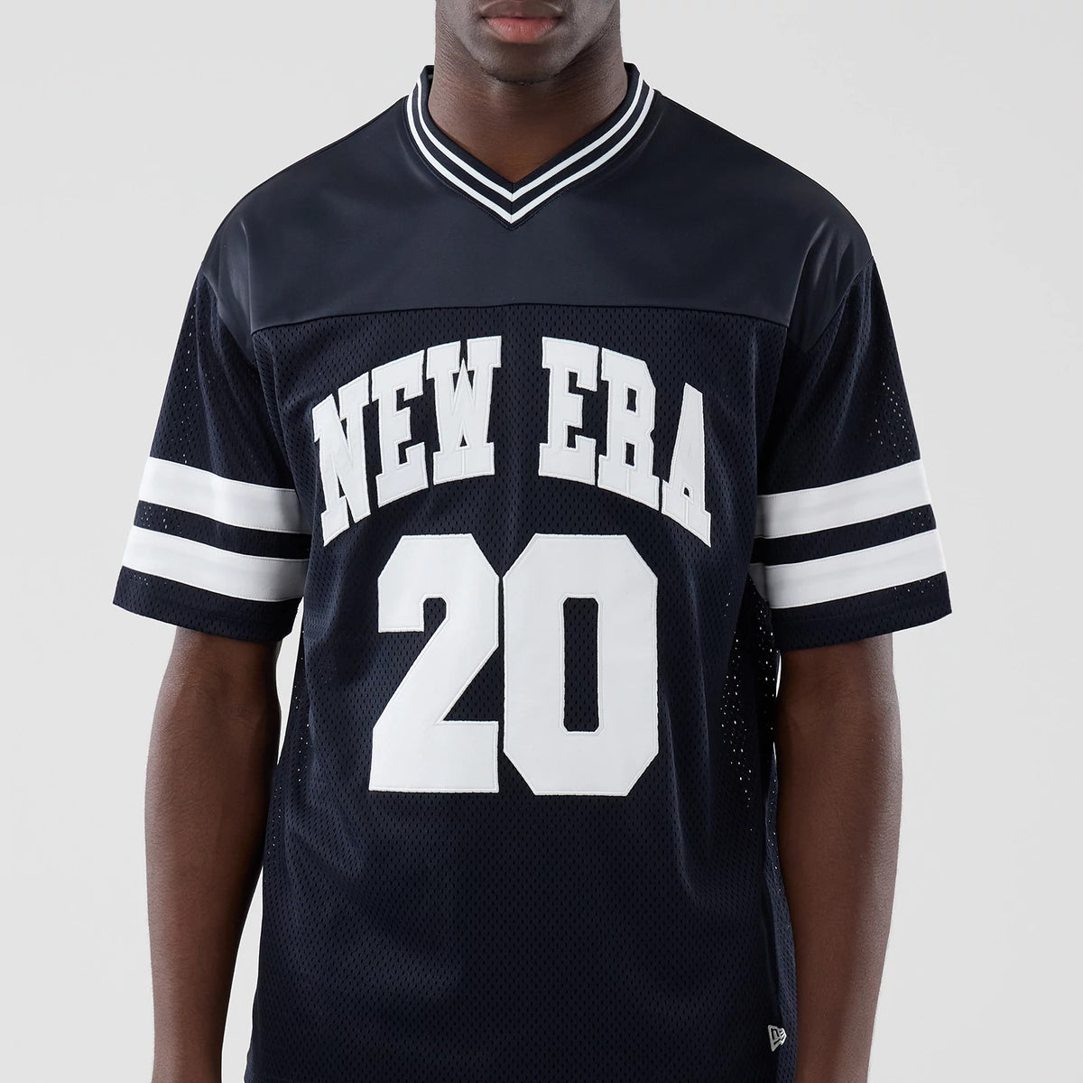 New Era Mesh Navy Oversized T-Shirt, front view on a model showcasing white printed New Era lettering across the chest, the number 20 below, and double white horizontal stripes on the sleeves, with a striped V-neck collar detail.