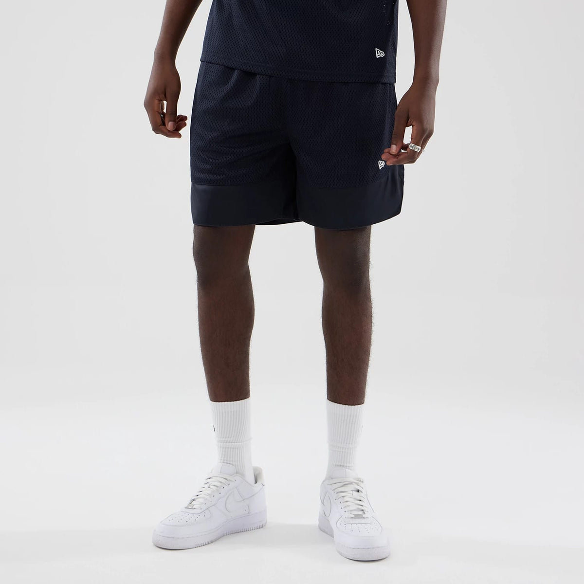 New Era Mesh Navy Oversized Shorts, front view on-model showcasing a loose fit with a slightly longer leg, contrasting solid navy hem, and small embroidered New Era flag logo near the left hem.