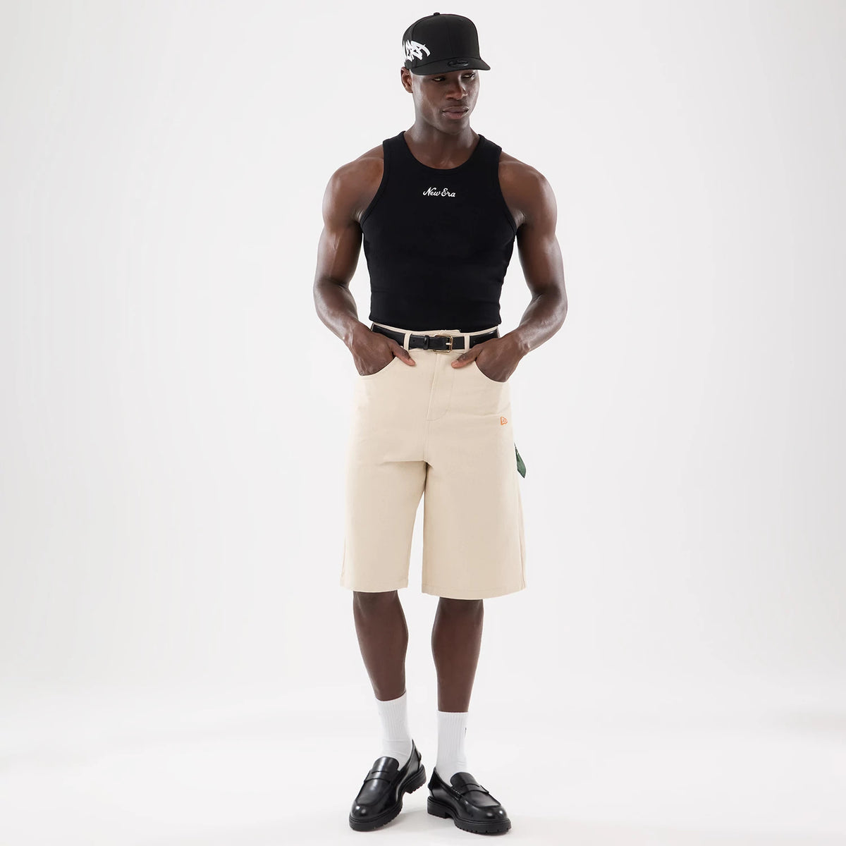 New Era Rib Black Vest, front view on a model wearing a black cap, featuring white embroidered New Era script across the chest, paired with beige shorts and black loafers for a casual yet refined look.