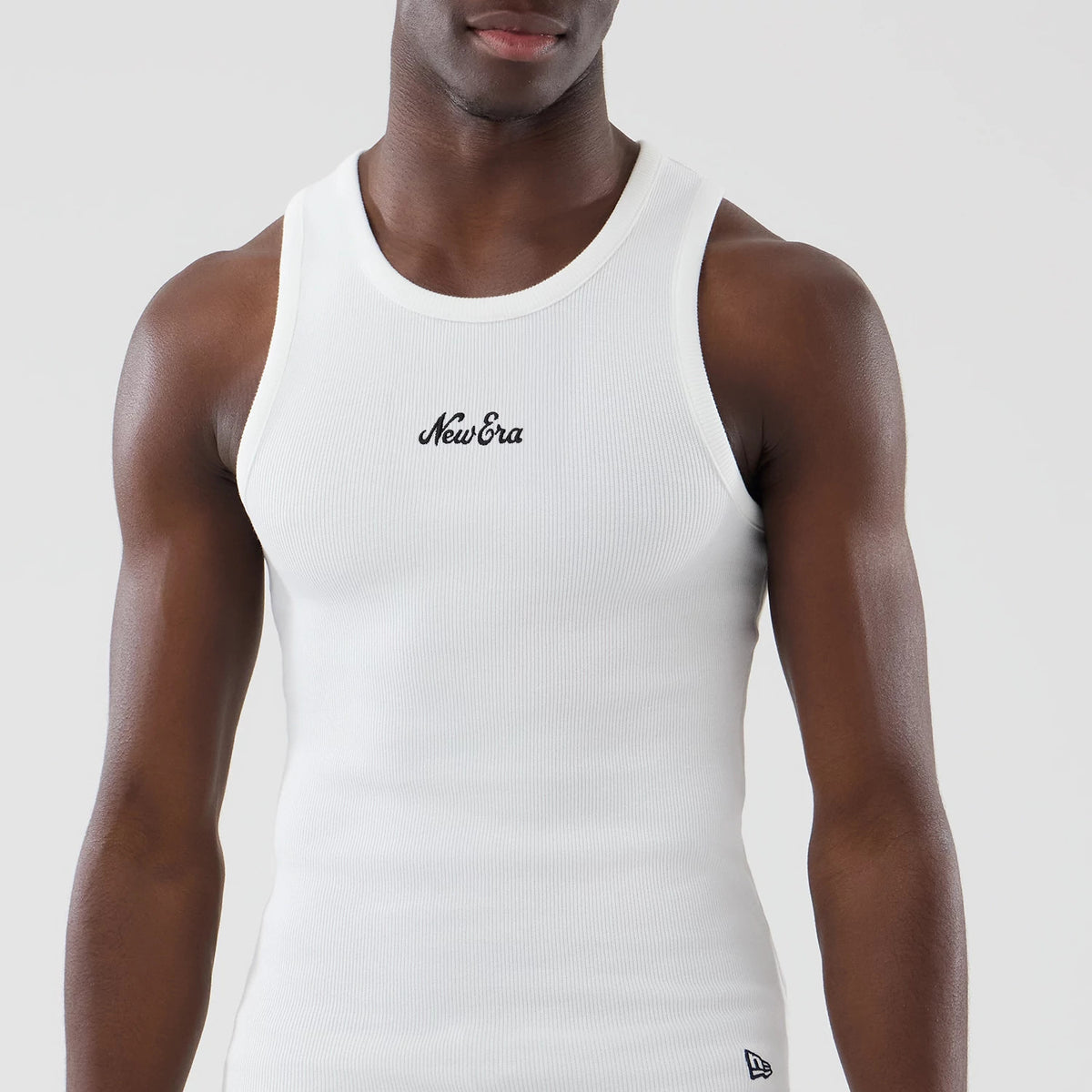 New Era Rib White Vest, front view on a model featuring a black embroidered New Era logo on the chest, a ribbed texture throughout the fabric, and a second New Era flag logo located at the lower hem.