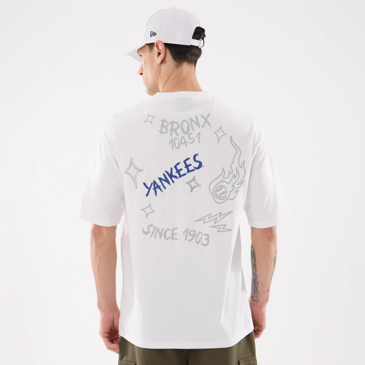 New Era New York Yankees MLB 59FIFTY Day Graphic White T-Shirt, back view on-model displaying blue embroidered Yankees lettering at the centre, surrounded by grey graphics including Bronx 10451 text, stars, a flaming baseball, and Since 1903.
