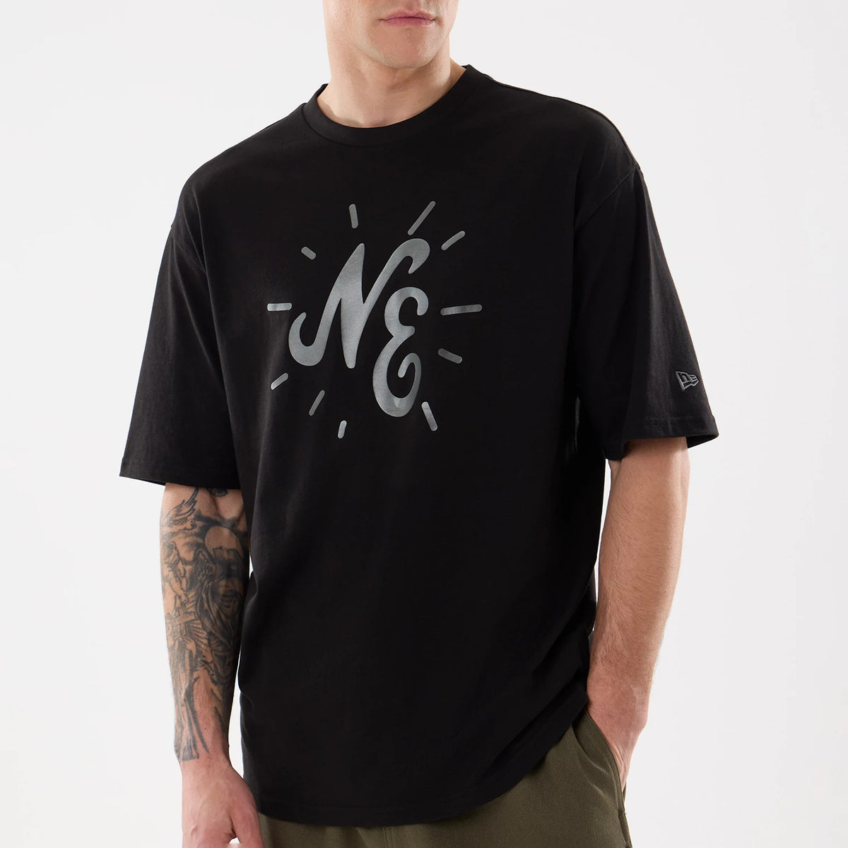 New Era 59FIFTY Day Graphic Black T-Shirt, front view on a model showing a large grey printed NE graphic with surrounding lines on the chest and a small embroidered New Era logo on the left sleeve.