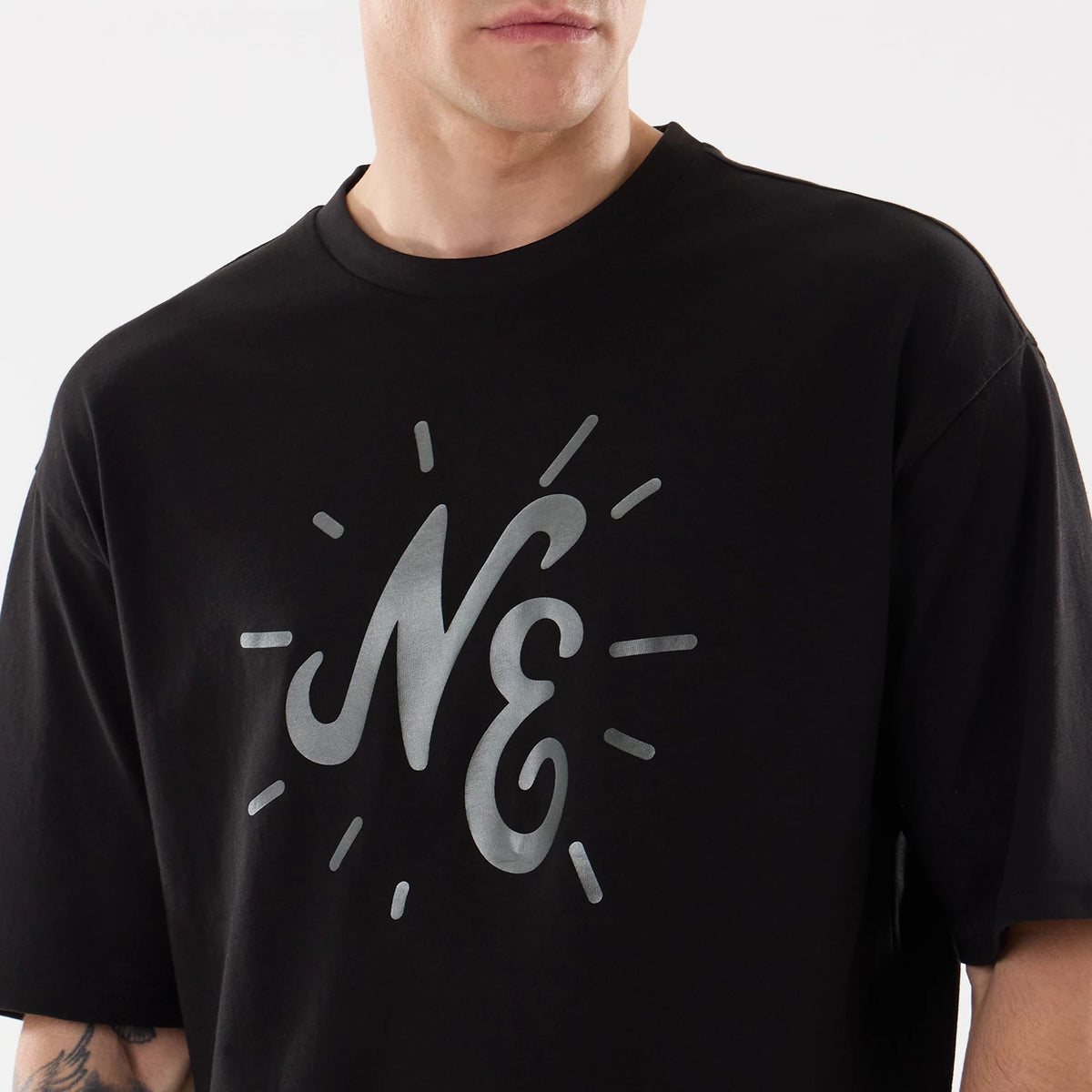 New Era 59FIFTY Day Graphic Black T-Shirt, front view on-model displaying a large, silver printed NE graphic centred on the chest, surrounded by radiating lines, short sleeves, and a crew neckline in a plain black design.