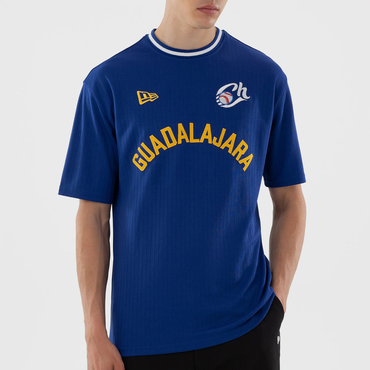 New Era Charros De Jalisco LMB Blue Oversized T-Shirt, front view showing a model with a blue shirt featuring yellow Guadalajara lettering across the chest, an embroidered New Era logo on the left, and a stylised baseball graphic on the right.