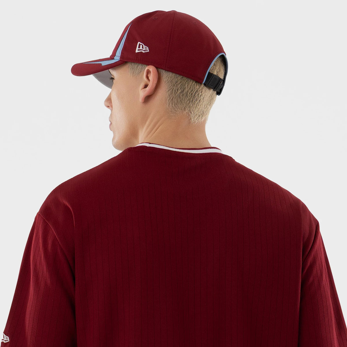 New Era Philadelphia Phillies MLB Dark Red Oversized T-Shirt, back view on a model paired with a matching dark red cap, showing the plain back of the oversized t-shirt with vertical lines and a New Era logo on the side of the cap.