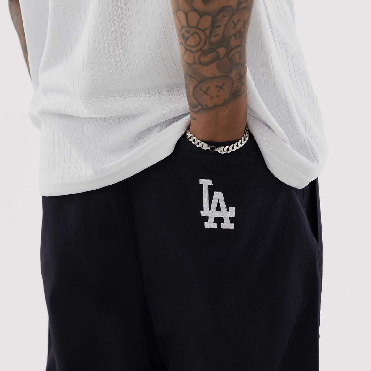 New Era LA Dodgers MLB Navy Woven Chinos, worn by a model with a white pinstripe shirt, showing the embroidered white LA logo on the front pocket area, highlighting the deep navy colour and tailored fit of the chinos.
