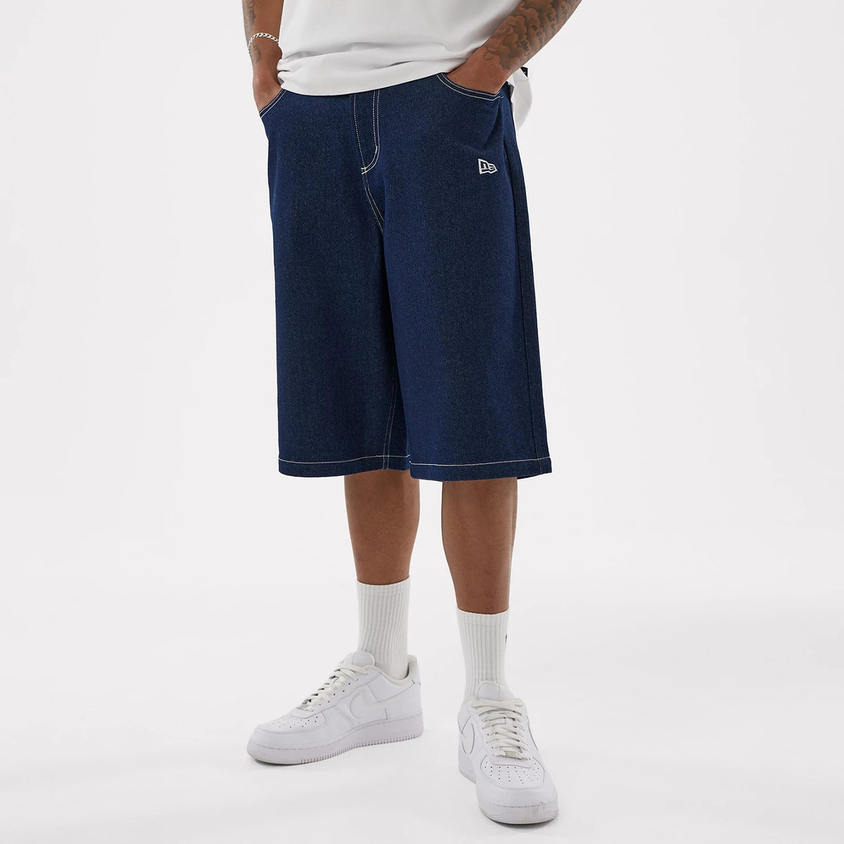 New Era LA Dodgers MLB Jort Dark Blue Oversized Shorts, front view on-model showing the wide-leg dark blue shorts with white stitching, side seam pockets, and an embroidered New Era logo on the front left thigh, styled with white trainers.