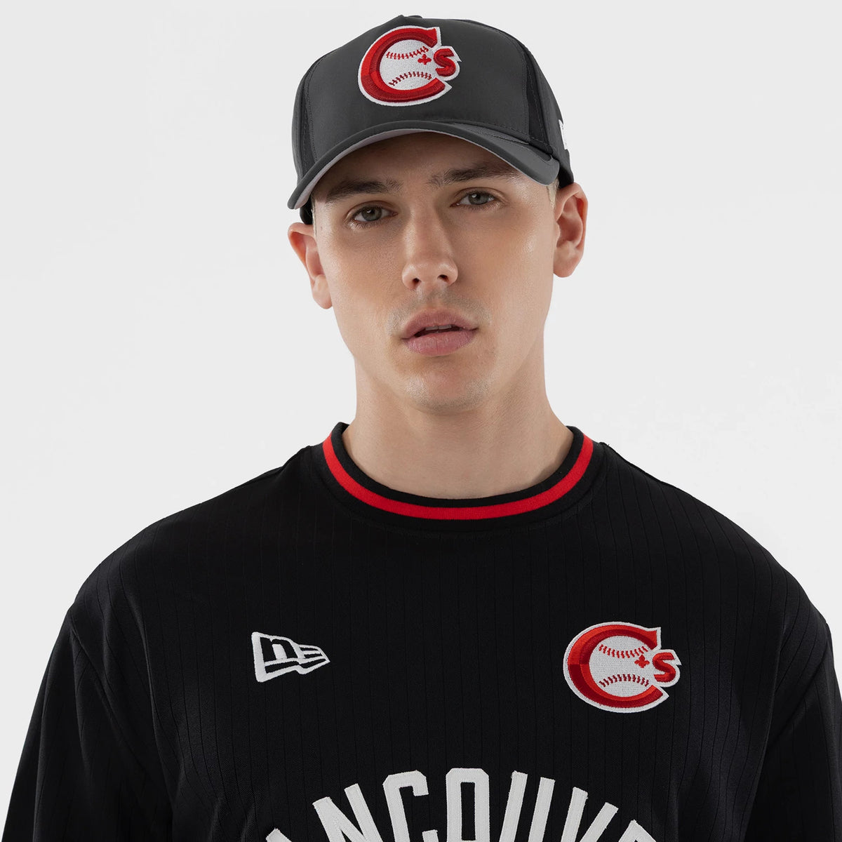 New Era Vancouver Canadians MiLB Black Oversized T-Shirt, front view on a model featuring a white embroidered New Era logo on the right chest, a red and white embroidered C with a baseball pattern on the left chest, and red on the neckline.