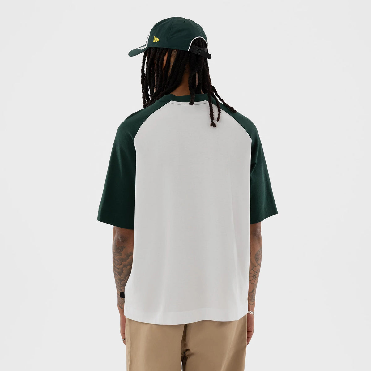 New Era Athletics MLB White Boxy T-Shirt, back view on a model wearing a matching cap, showing a plain white back with contrasting green sleeves and a dark green collar, with the New Era logo embroidered on the side of the cap.