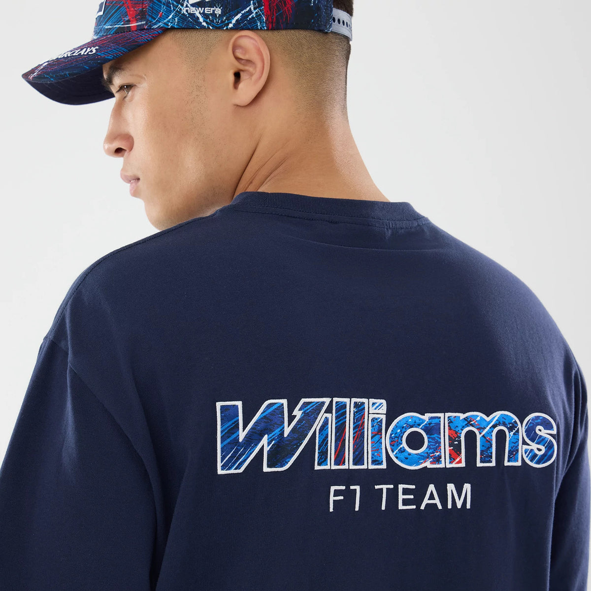 New Era Williams GB Race Special Navy T-Shirt, back view on-model showing the embroidered Williams F1 Team lettering in white and blue across the upper back, paired with a matching New Era cap featuring a colourful pattern and eyelets.