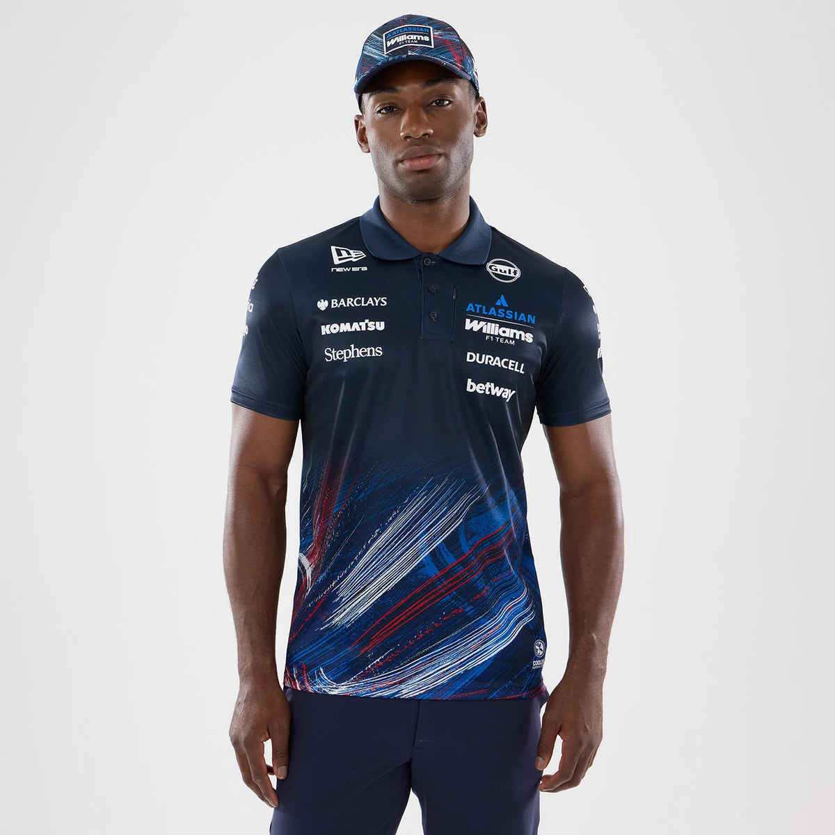 New Era Williams GB Race Special Navy Tech Polo T-Shirt, front view on a model wearing a matching cap, showing various sponsor logos printed across the chest and sleeves, with dynamic red and blue graphic accents at the hem.