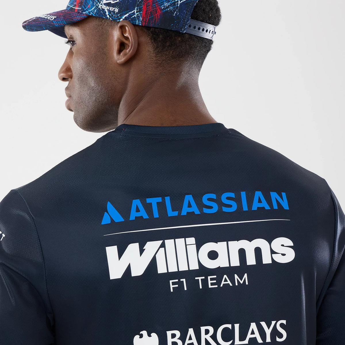 New Era Williams GB Race Special Tech Navy T-Shirt, back view on a model wearing a colourful cap, featuring Atlassian and Williams F1 Team logos printed in blue and white across the upper back, with additional sponsor logos below.