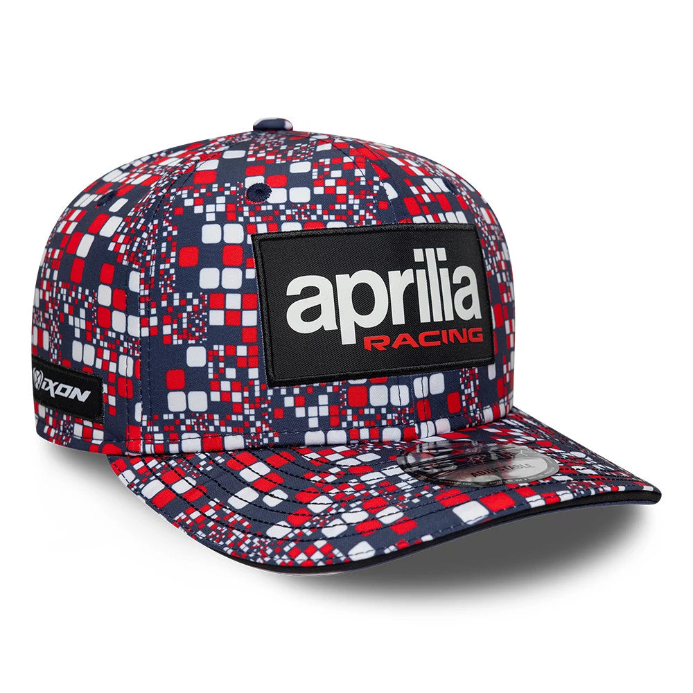 Aprilia Replica Silverstone Race Special Blue New Era 9SEVENTY Stretch Snap Adjustable Cap, front view showing a black patch with white and red aprilia racing embroidery, multicoloured geometric pattern across the panels and visor.