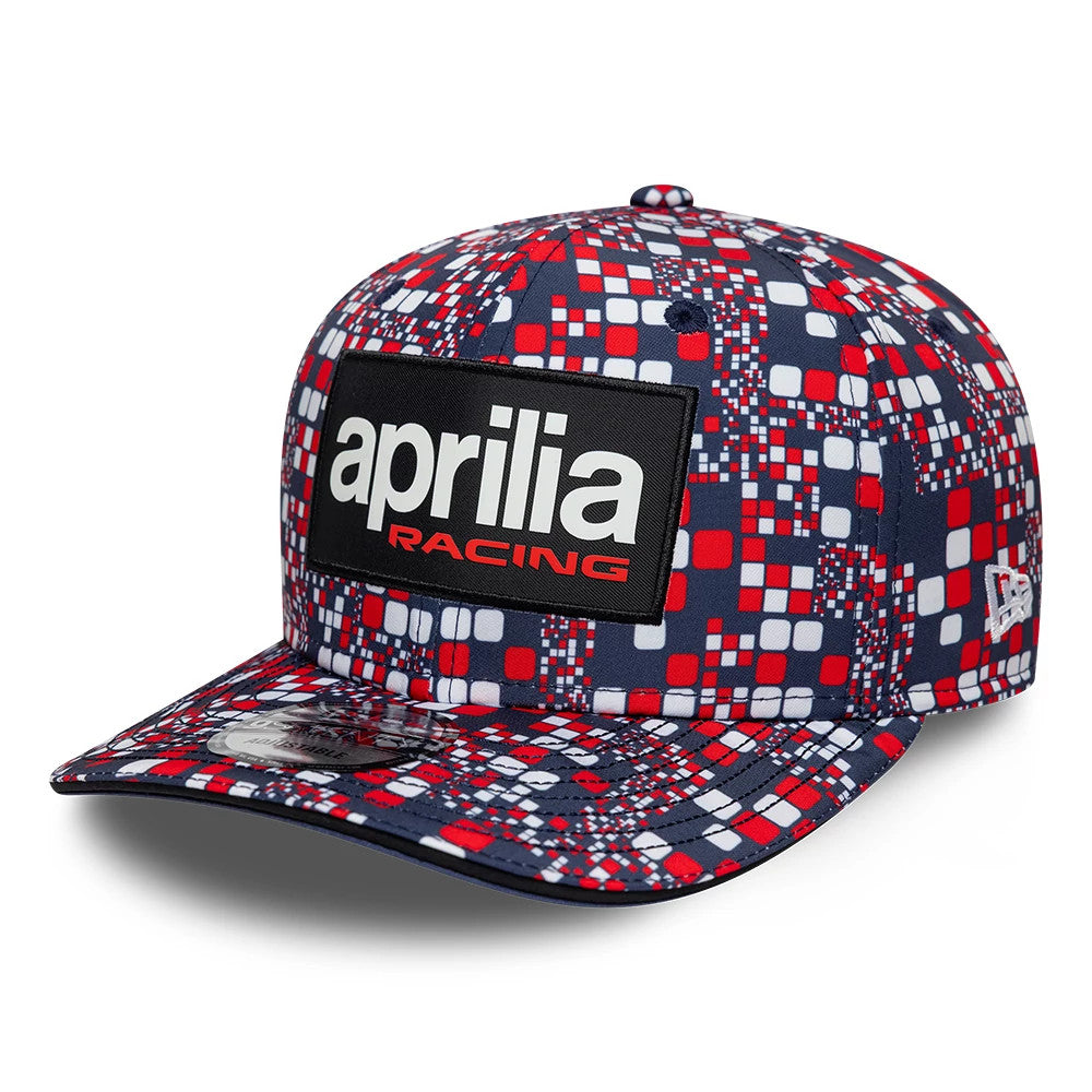 Aprilia Replica Silverstone Race Special Blue New Era 9SEVENTY Stretch Snap Adjustable Cap, three-quarter view showing a large black and white 'aprilia racing' patch on the front panel, red and blue geometric pattern.