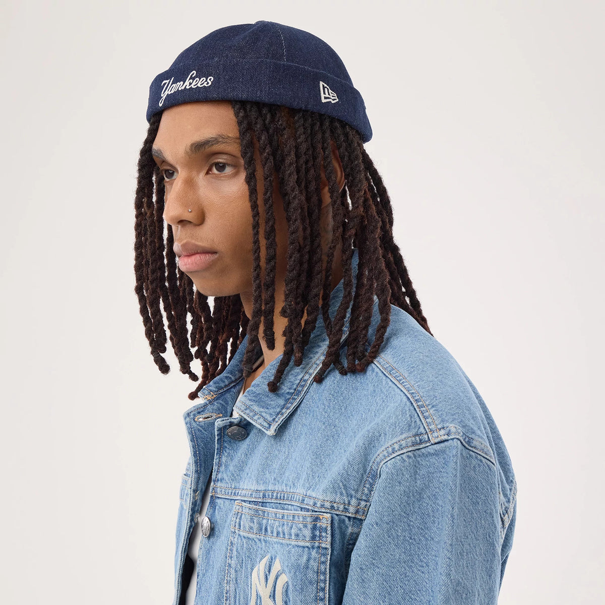 New Era New York Yankees MLB Denim Skully Navy Docker Adjustable Cap, on-model side view paired with a denim jacket, showing white Yankees script embroidery on the front, with a New Era flag logo embroidered on the left side of the cap.