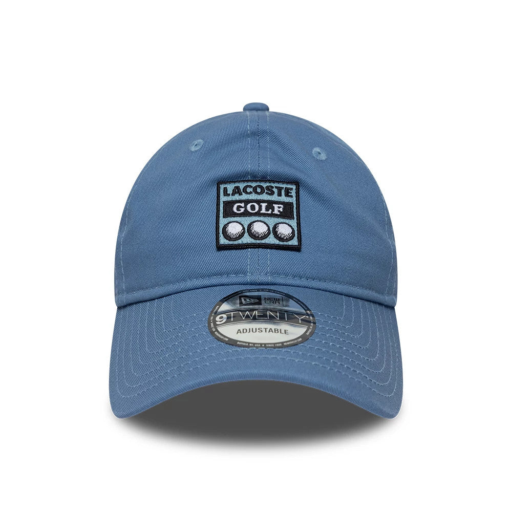 Lacoste X New Era Blue 9TWENTY Adjustable Cap, front view showing a black and white Lacoste Golf patch with three golf balls on the structured blue crown, and a 9TWENTY size sticker on the curved blue visor.