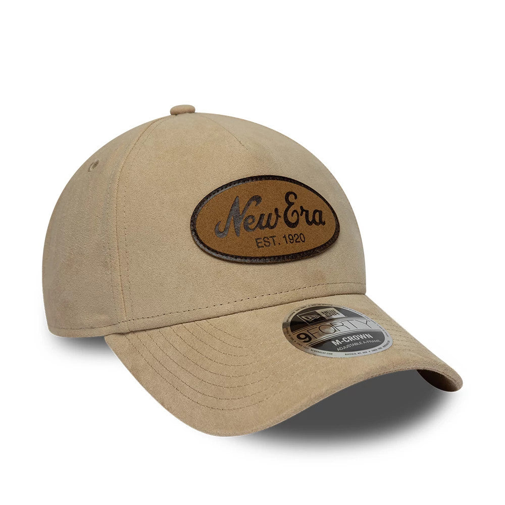 New Era Faux Suede Light Beige 9FORTY M-Crown A-Frame Adjustable Cap, three-quarter view showing a raised brown New Era oval logo embroidered on the front panel, light beige visor, and 9FORTY size sticker on the top of the visor.