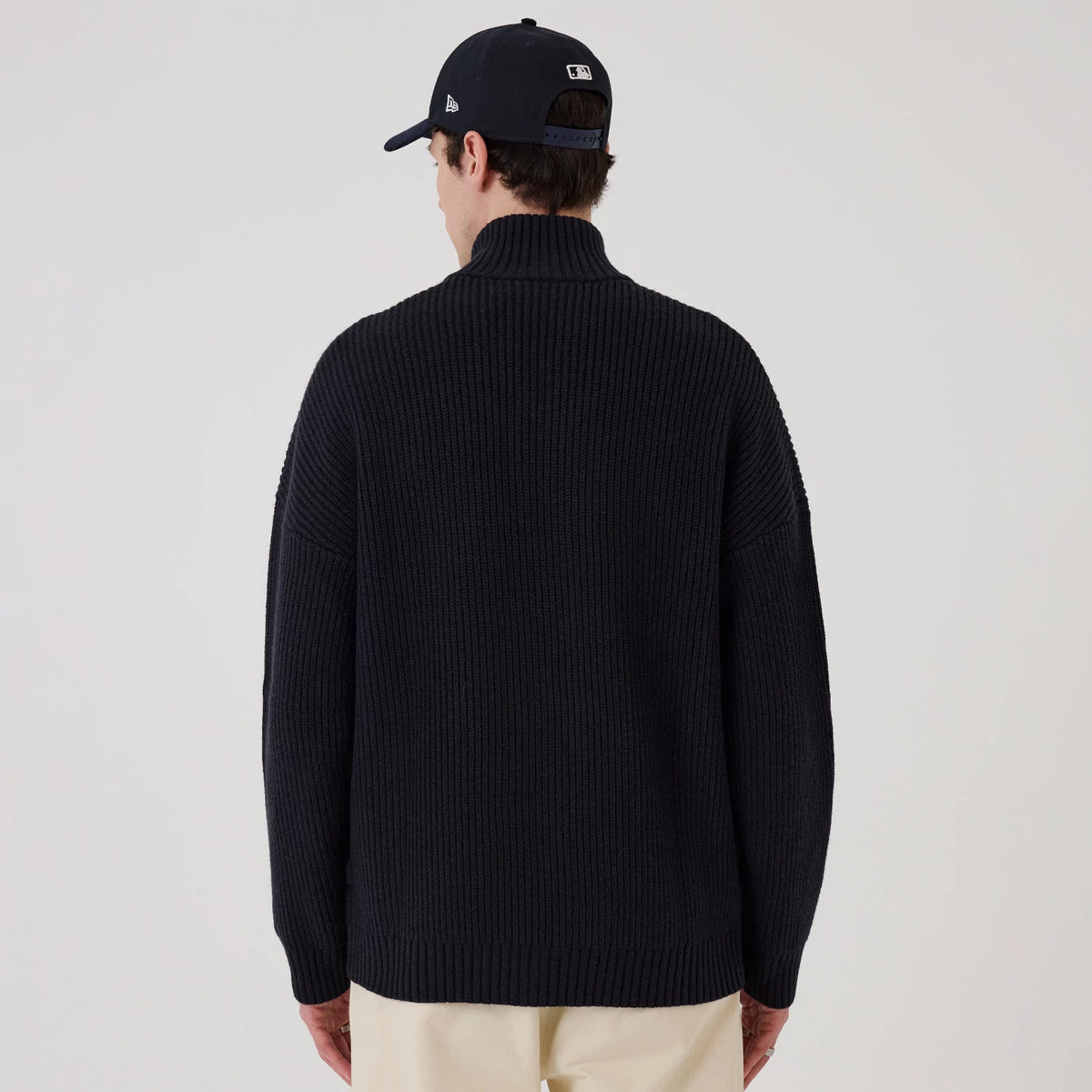 New Era New York Yankees MLB Navy 2 Way Zip Cardigan, rear view on a model wearing a navy cap, showing the ribbed texture and high collar of the dark navy cardigan, with dropped shoulder seams and loose-fitting sleeves.