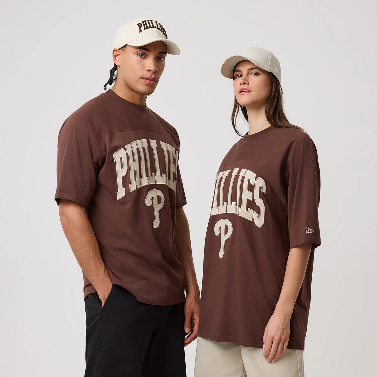 New Era Philadelphia Phillies MLB Arch Graphic Brown Oversized T-Shirt, front view on models showing the large embroidered Phillies lettering and logo on the chest, with the New Era logo embroidered on the left sleeve, styled with light.