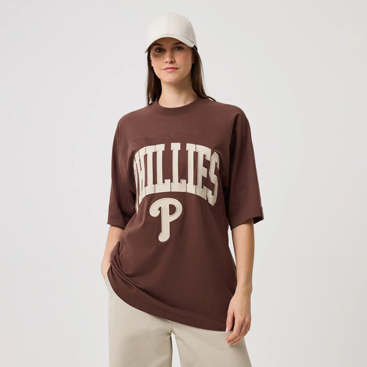 New Era Philadelphia Phillies MLB Arch Graphic Brown Oversized T-Shirt, front view on a model with a neutral cap, showing large cream embroidered PHILLIES lettering across the chest with a prominent P logo underneath on the relaxed brown fit.