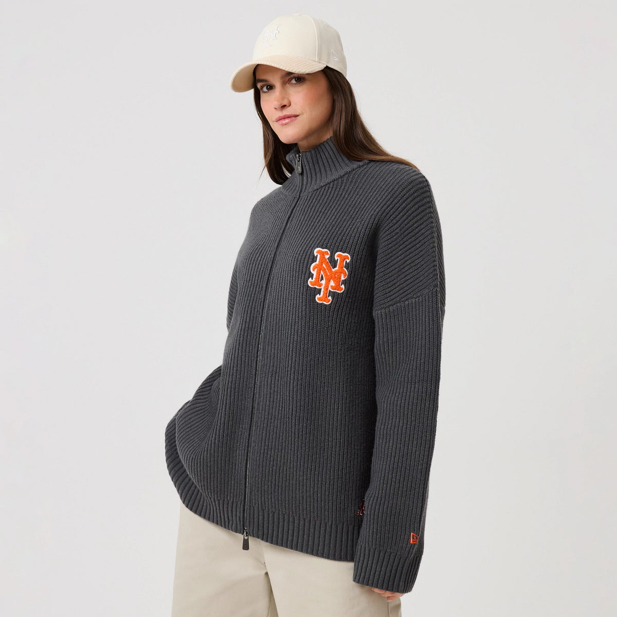 New Era New York Mets MLB Charcoal 2 Way Zip Cardigan, front view on a model showing the ribbed texture and prominent orange NY logo embroidered on the left chest, with a high collar and a New Era flag logo on the left sleeve cuff.