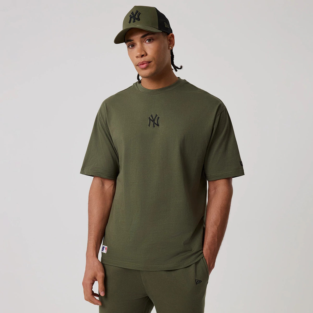 New Era New York Yankees MLB League Essential Green Oversized T-Shirt, front view on-model featuring a black embroidered New York Yankees logo centred on the chest, styled with a matching green cap also displaying the Yankees logo on the front panel.