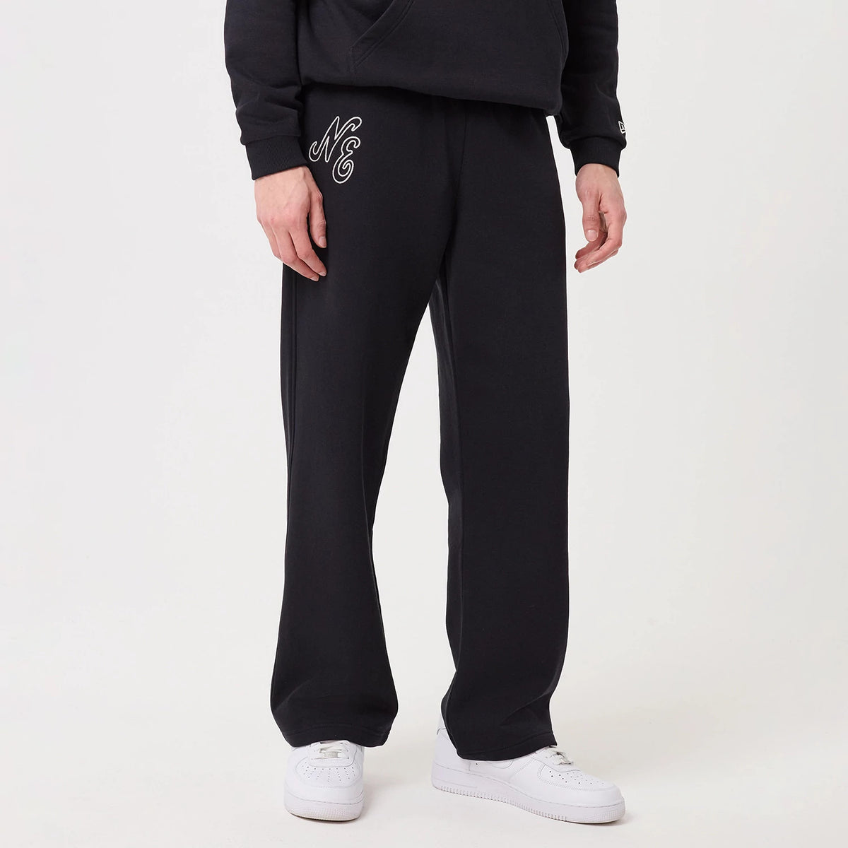 New Era Navy Straight Leg Joggers, front view on a model wearing a black hoodie and white trainers, featuring the embroidered NE logo on the left thigh, wide leg opening, and a relaxed fit.