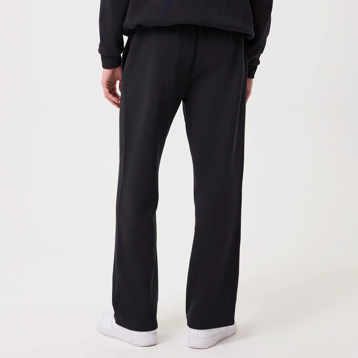 New Era Navy Straight Leg Joggers, rear view on a model showing the relaxed fit falling naturally from the waist to the hem, with a straight leg design, elasticated waistband, and neat ankle cuffs paired with white sneakers.
