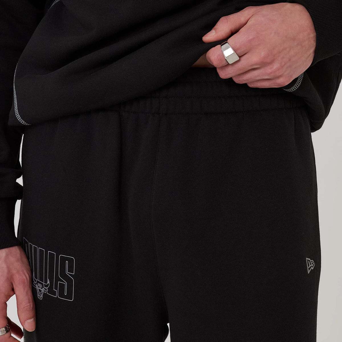 New Era Chicago Bulls NBA Graphic Black Straight Leg Joggers, close-up view showing the white Bulls logo printed on the left leg, an elasticated waistband for comfort, and the New Era flag logo embroidered in white on the right hip.