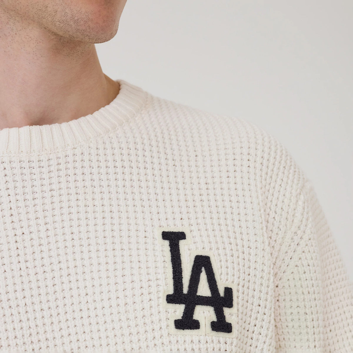 New Era LA Dodgers MLB Waffle Knit Open White Crew Neck Sweater, front view on a model showing the textured white waffle knit fabric, ribbed crew neck collar, and the black LA Dodgers logo embroidered on the left chest.