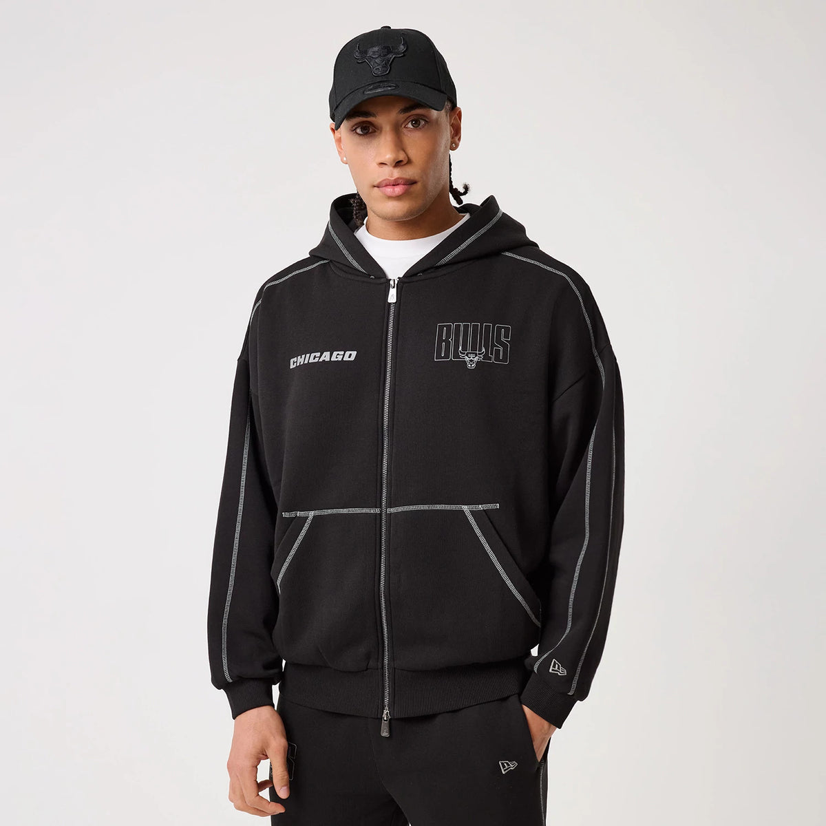 New Era Chicago Bulls NBA Graphic Black Pullover Hoodie, front view on a model with a black cap, featuring a zip front, embroidered Chicago logo on the left chest, Bulls text with a bull graphic on the right, and contrast piping on the sleeves.
