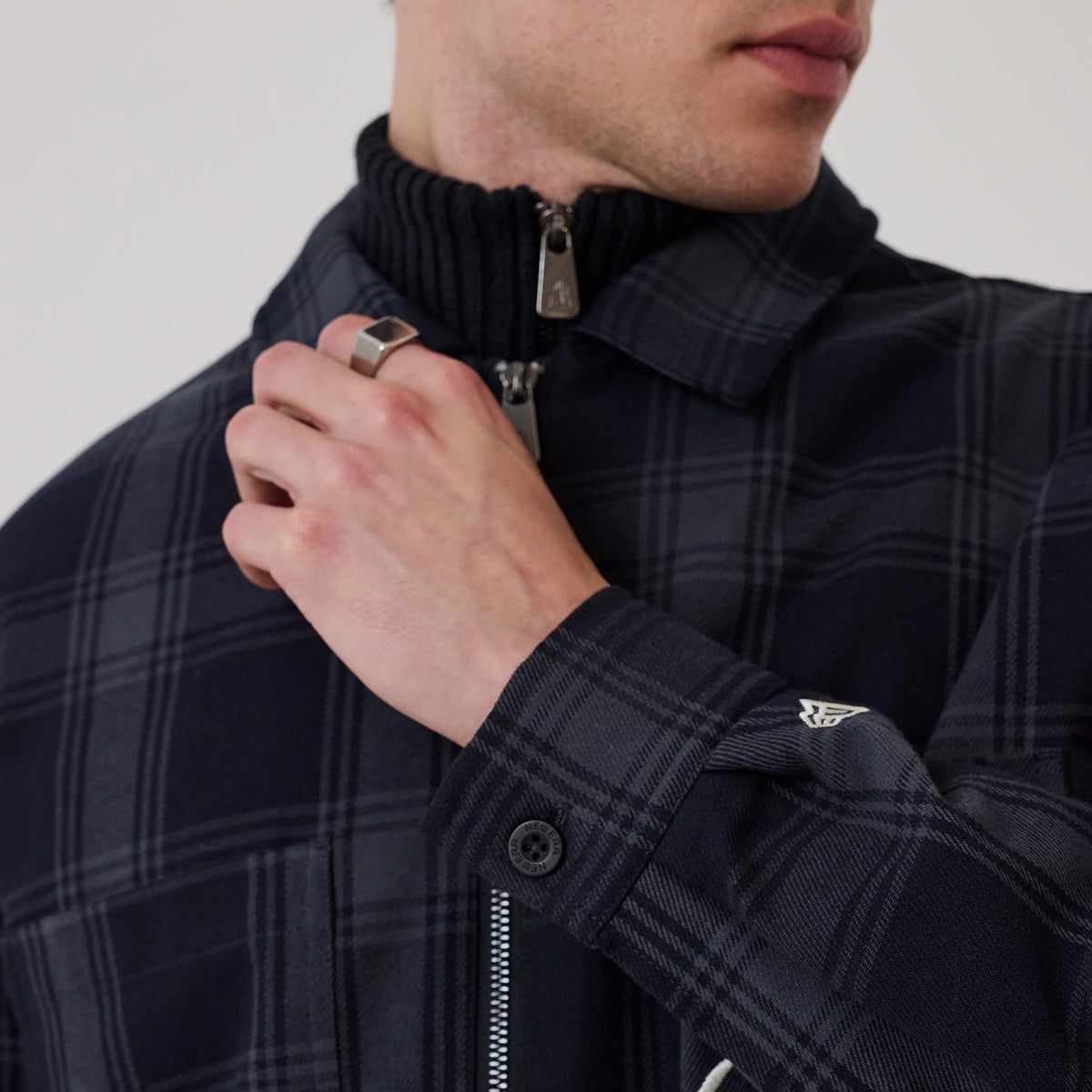 New Era Navy Shacket, front view on a model showing the dark blue check pattern, silver zip closure with a black ribbed neckline underneath, and the New Era flag logo embroidered at the cuff of the sleeve.