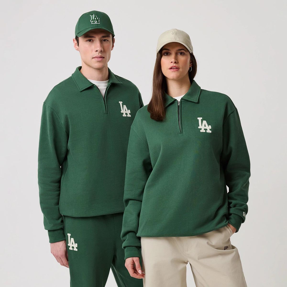 New Era LA Dodgers MLB Dark Green 1/4 Zip Sweater, front view on a model with matching dark green joggers and a cap, showing the white LA logo embroidered on the left chest and a half-zip design under the collar.