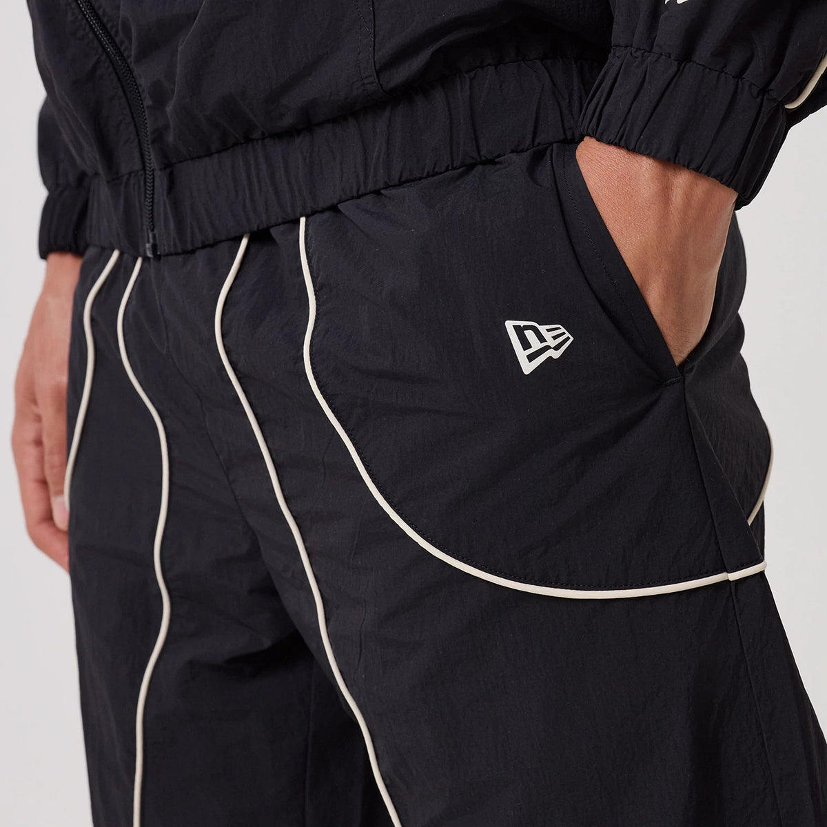 New Era New York Yankees MLB Piping Navy Track Pants, side view showing white piping detail running vertically along the leg, New Era flag logo embroidered on the left pocket, and a relaxed fit with an elastic waistband.