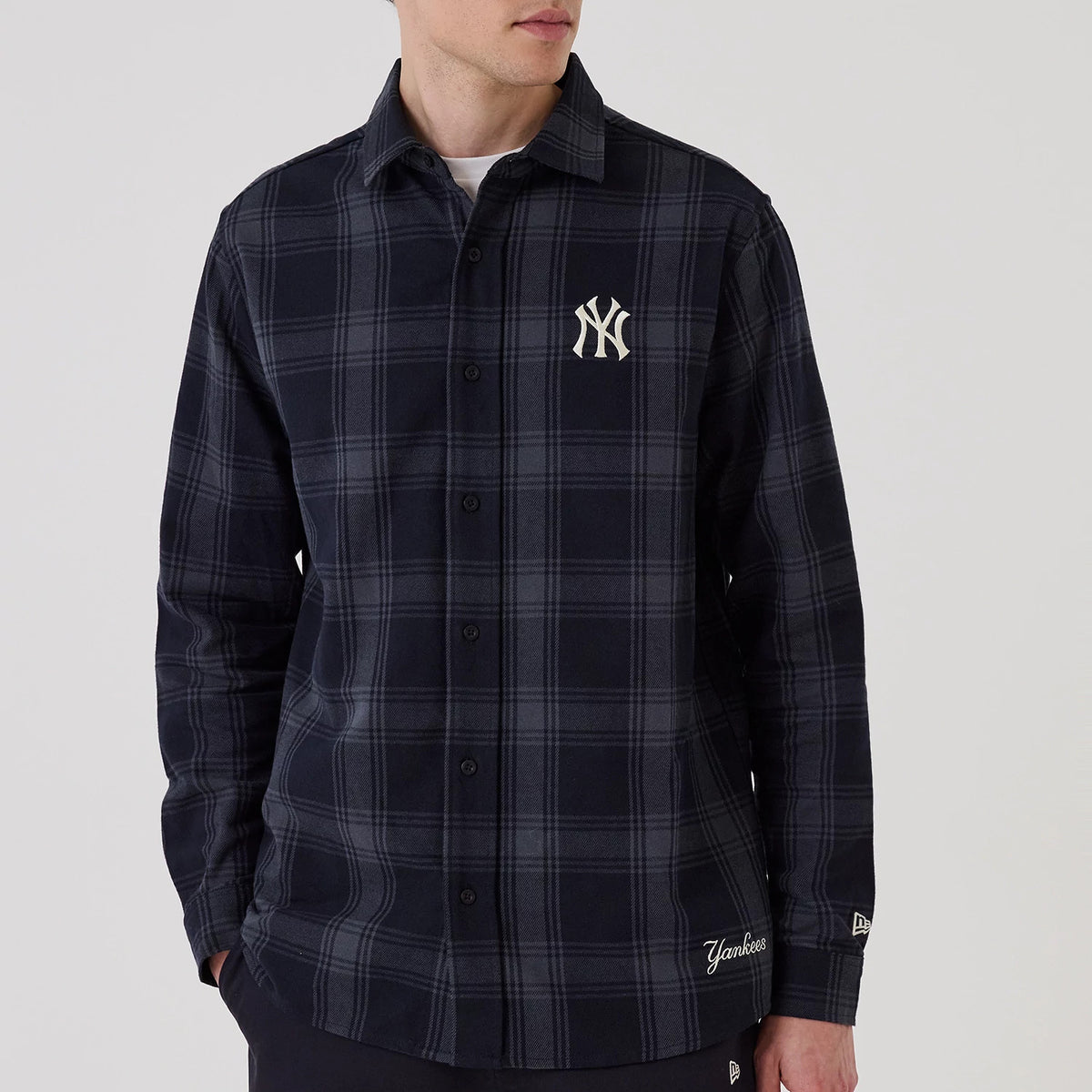 New Era New York Yankees MLB Plaid Navy Long Sleeve Shirt, front view on a model showing the white embroidered NY logo on the left chest, button-down collar and plaid pattern in shades of navy with Yankees lettering above the hem.