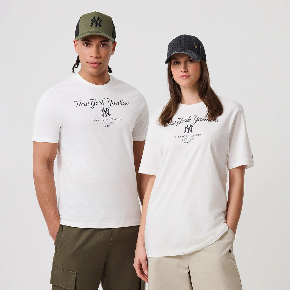 New Era New York Yankees MLB Linear White T-Shirt, front view on-model featuring elegant script New York Yankees text and navy NY logo on the chest, worn with neutral trousers and styled with matching New Era caps in contrasting colours.