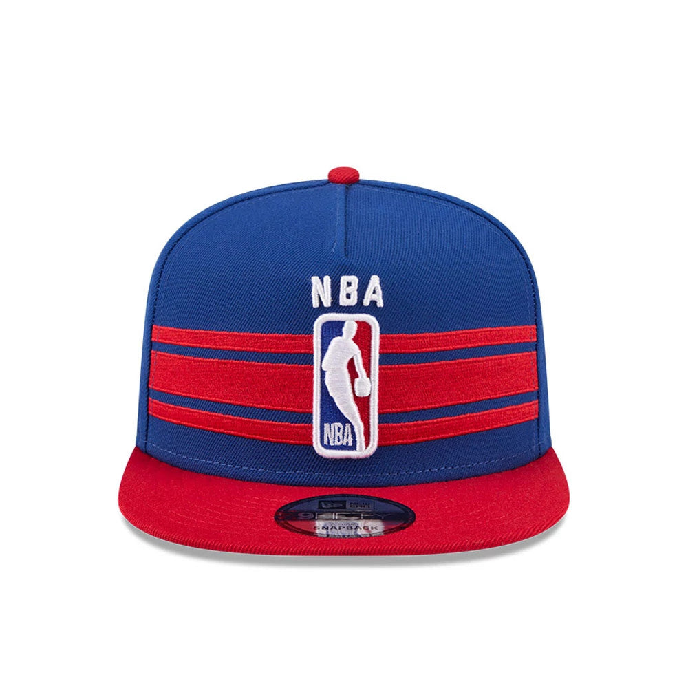 NBA Logo NBA Tip Off 2026 Blue New Era 9FIFTY A-Frame Snapback Adjustable Cap, front view showing the raised white NBA logo embroidered on the structured blue crown with red horizontal stripes and a red flat visor, featuring a 9FIFTY size sticker.