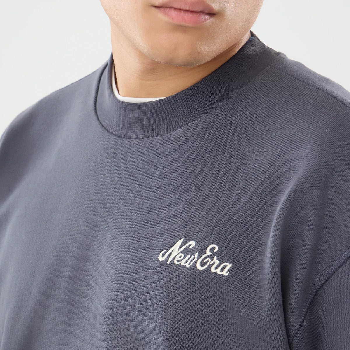 New Era Open Hem Dark Grey Oversized Crew Neck Sweater, three-quarter view on a model showing the embroidered New Era script logo on the left chest, ribbed crew neck collar, and relaxed fit with a dark grey colour.