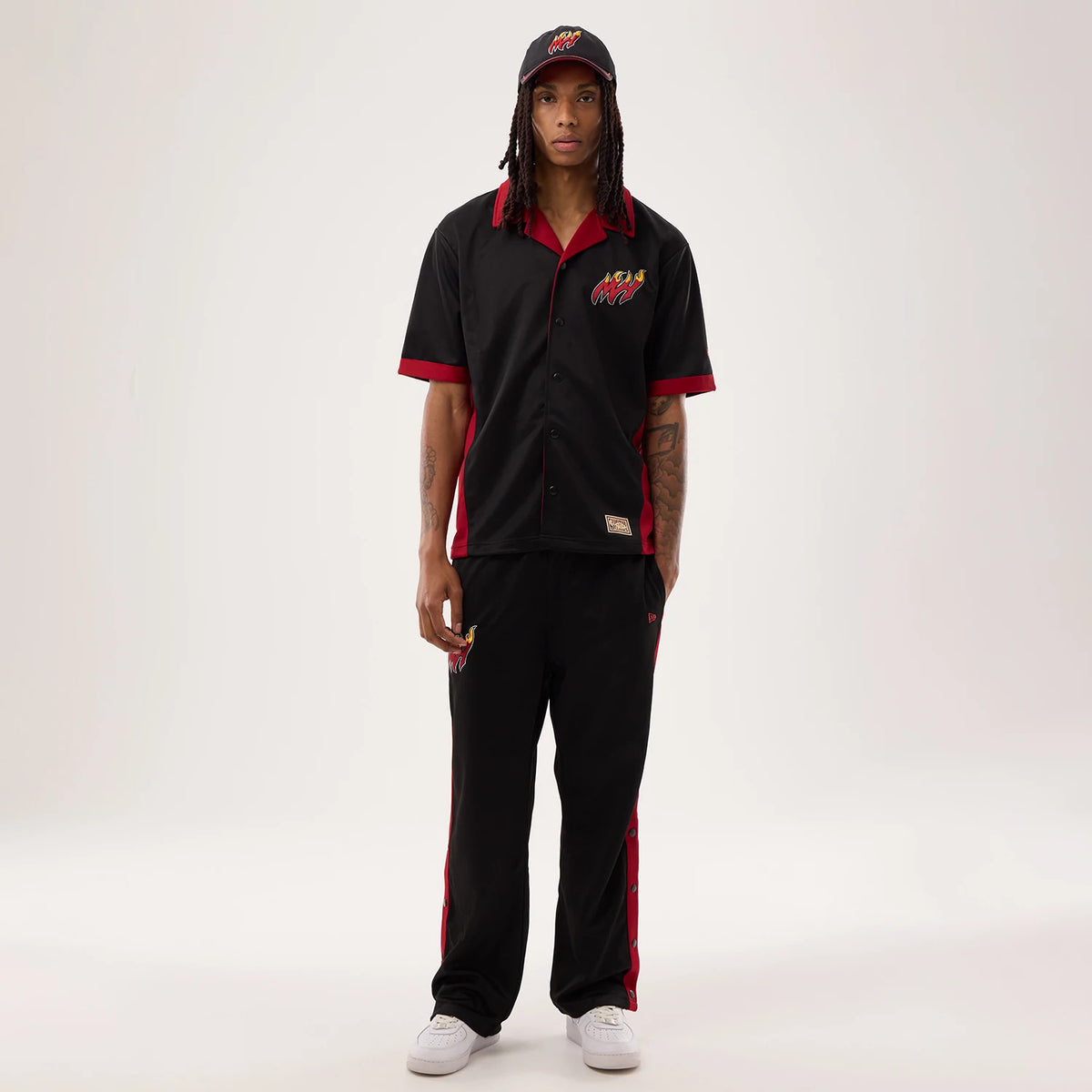 New Era Miami Heat NBA Hardwood Classic Revere Black Short Sleeve Shirt, front view on a model wearing matching black trousers and cap, featuring red accents at the collar and sleeves, with the Miami Heat logo embroidered on the left chest.